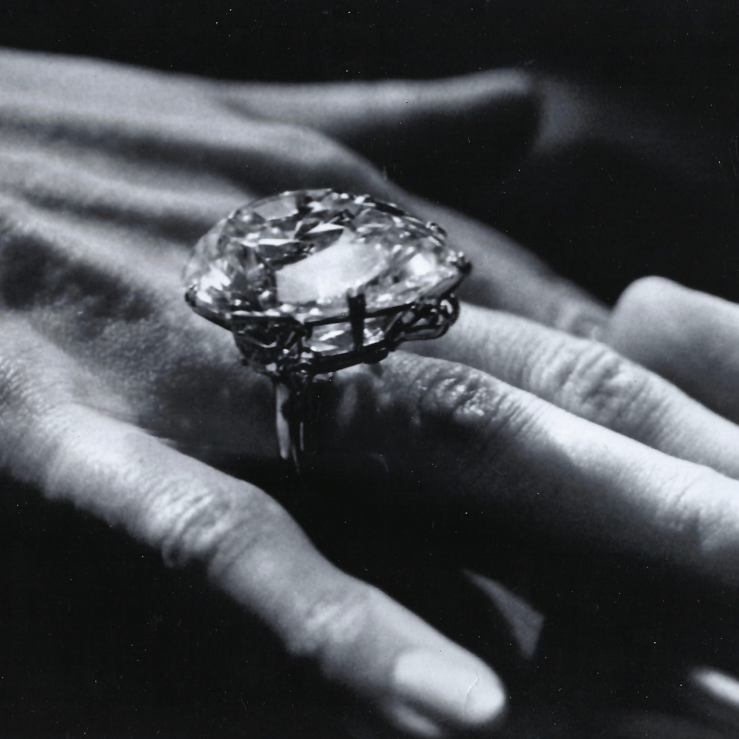 Hand wearing a large, cushion-cut diamond ring with an intricate setting.