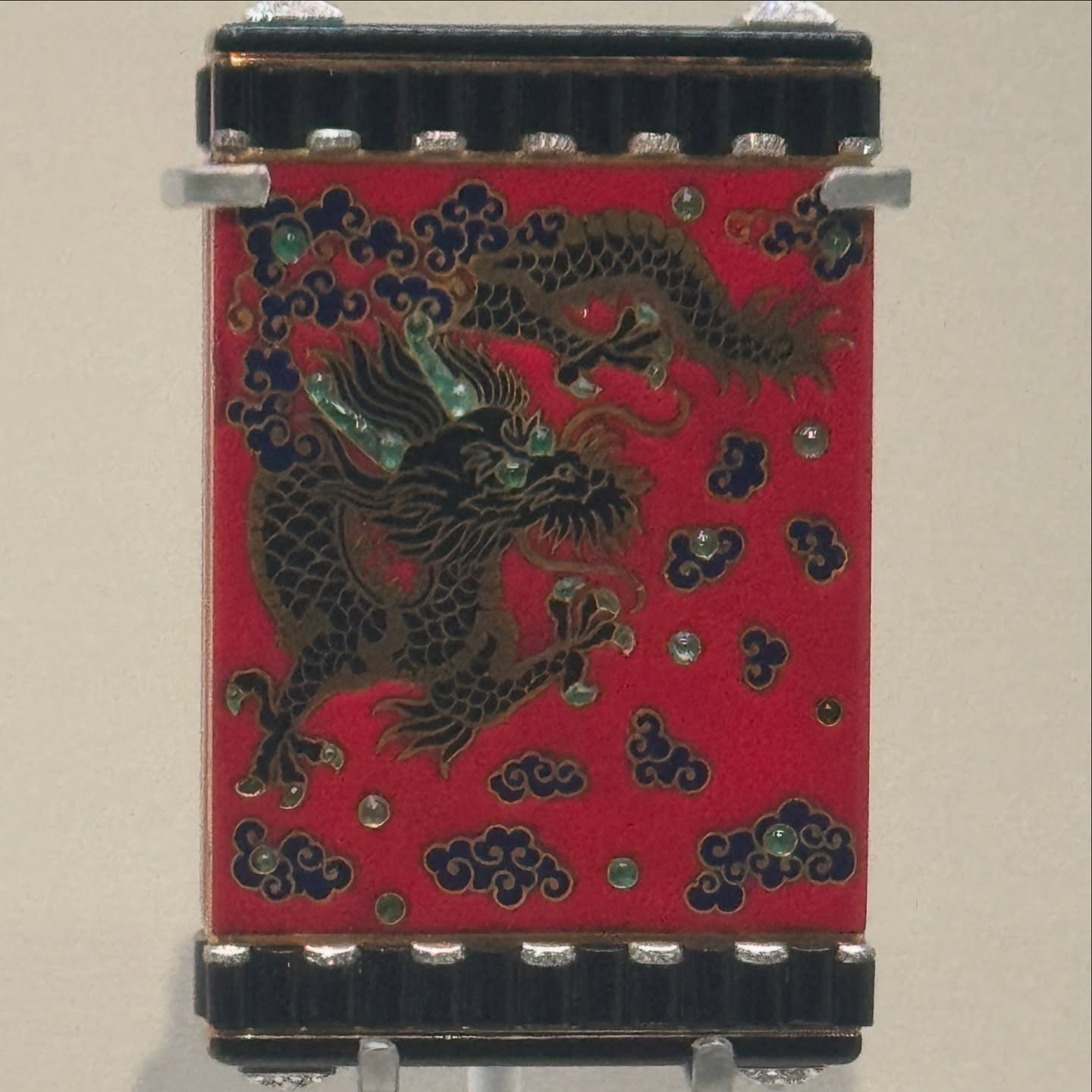 Cartier red enamel object with black and gold dragon, blue clouds, gemstones, and onyx trim.