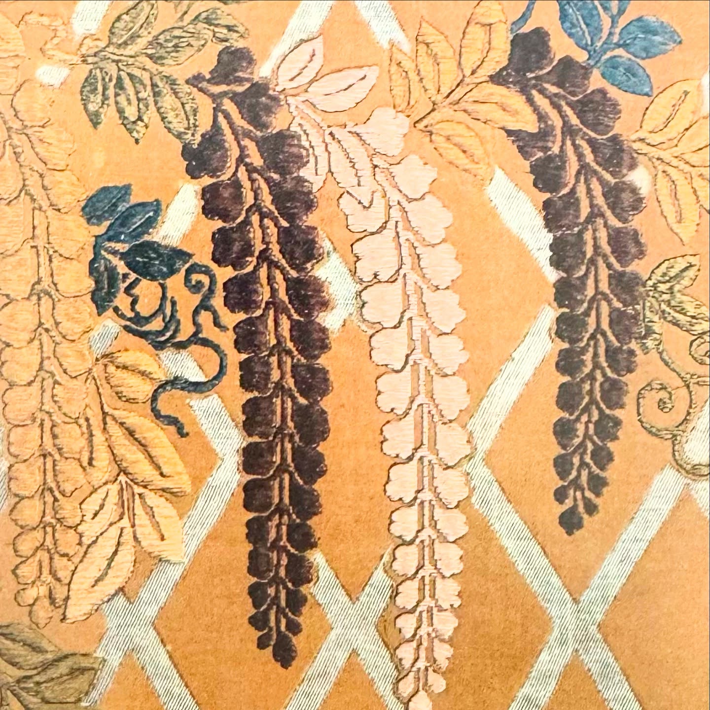 Textile with golden background, diagonal grid, and colorful wisteria floral pattern.