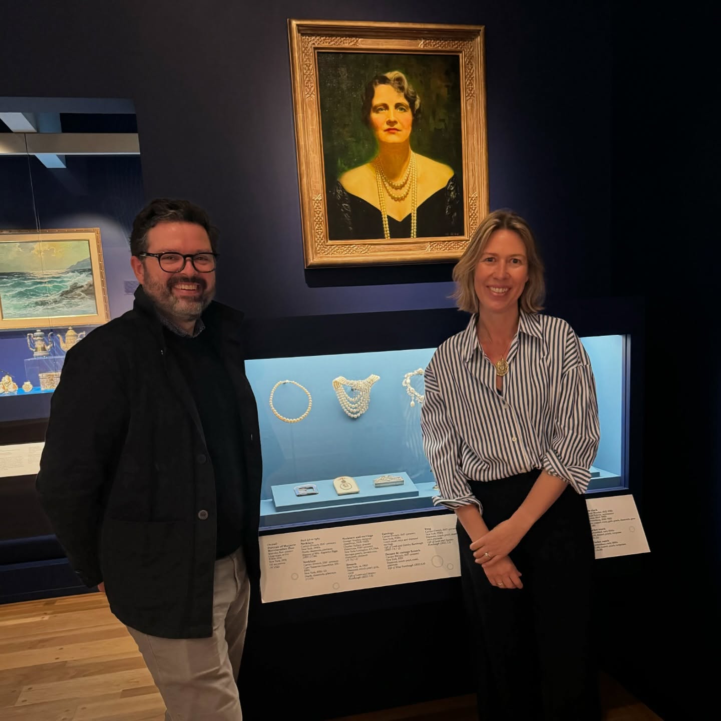 Francesca Cartier Brickell and a man in a museum, with a portrait and display of pearl jewellery.