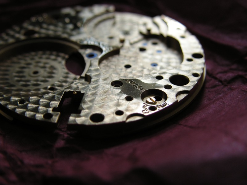 Close-up of perlage on a watch movement main plate — the circular brushed finish characteristic of fine watchmaking