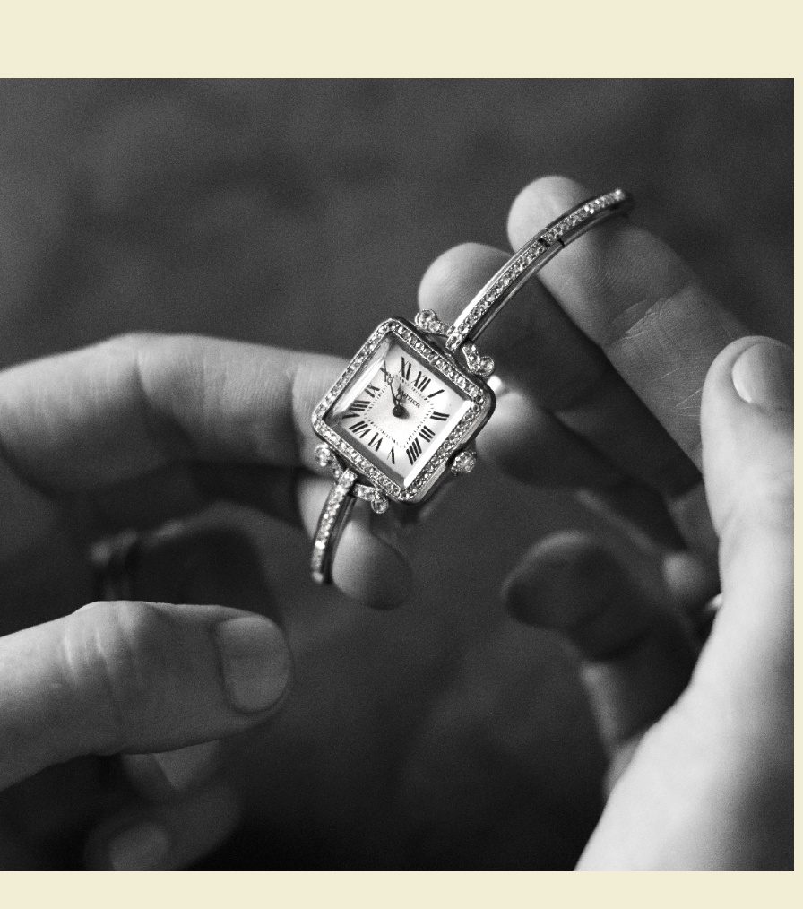 A delicate vintage Cartier watch with a square diamond-encrusted face and Roman numerals, held between two hands in black and white.
